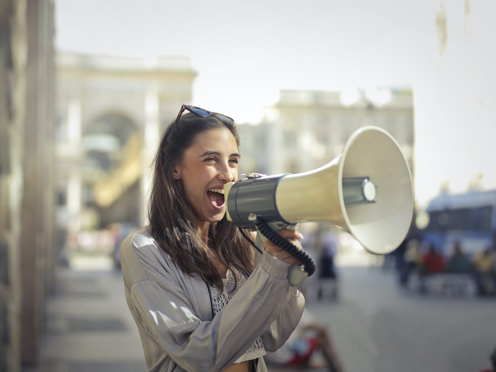 Cheerful young woman in a casual outfit shouting into a megaphone on a sunny day.