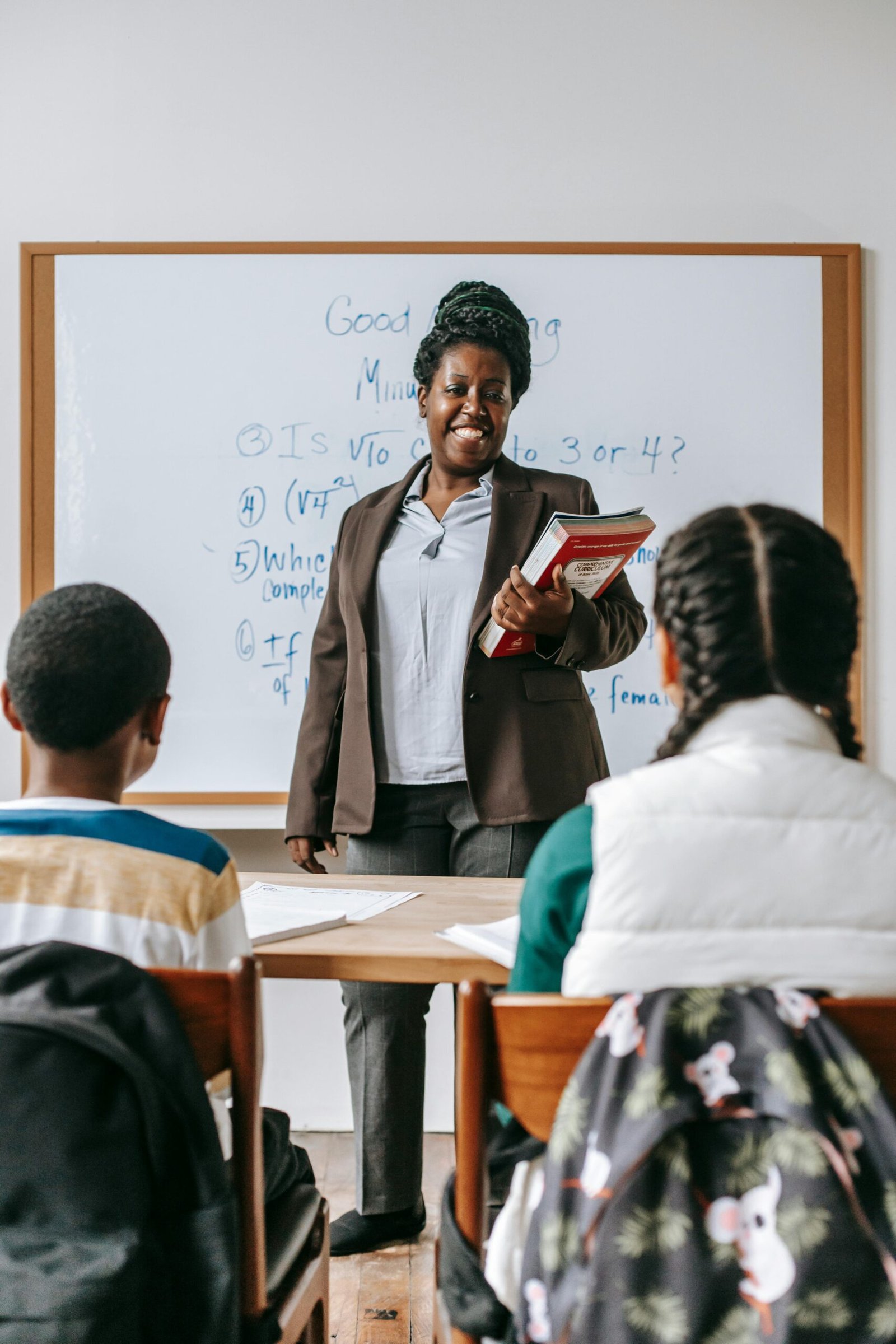 Back view of focused kids sitting at desk in classroom and listening to African American teacher against whiteboard