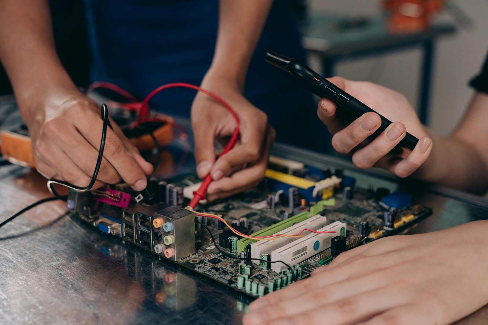 Close-up of hands working on a motherboard using electrical tools and tester.